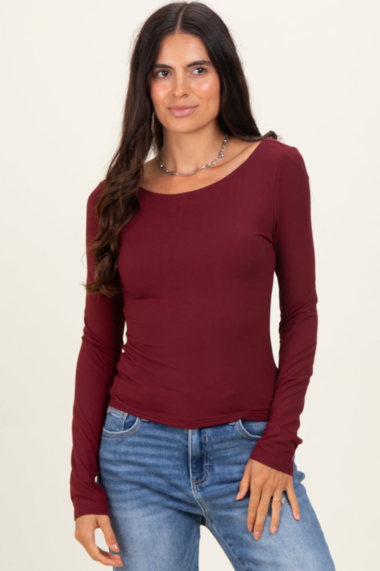 woman wearing a burgundy long sleeve fitted top with a scoop neckline and light blue jeans