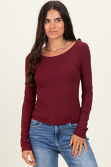 woman wearing a burgundy long sleeve fitted top with a scoop neckline and light blue jeans