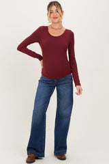 woman wearing a burgundy long sleeve maternity top and flare jeans, showing a visible baby bump