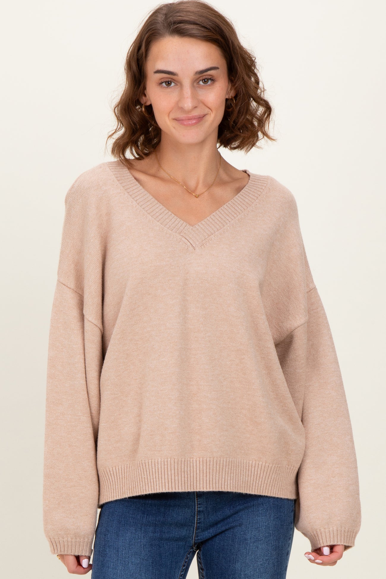 woman wearing a beige oversized v-neck sweater with long sleeves and relaxed fit, paired with blue jeans