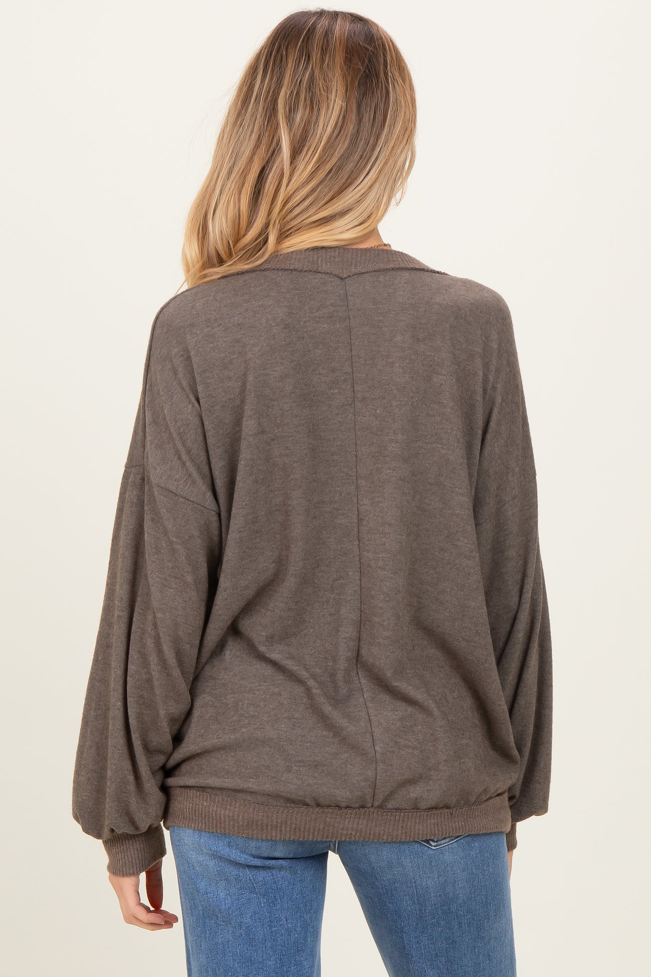 woman wearing a brown oversized maternity sweater with long sleeves, showing the back view and styled with blue jeans