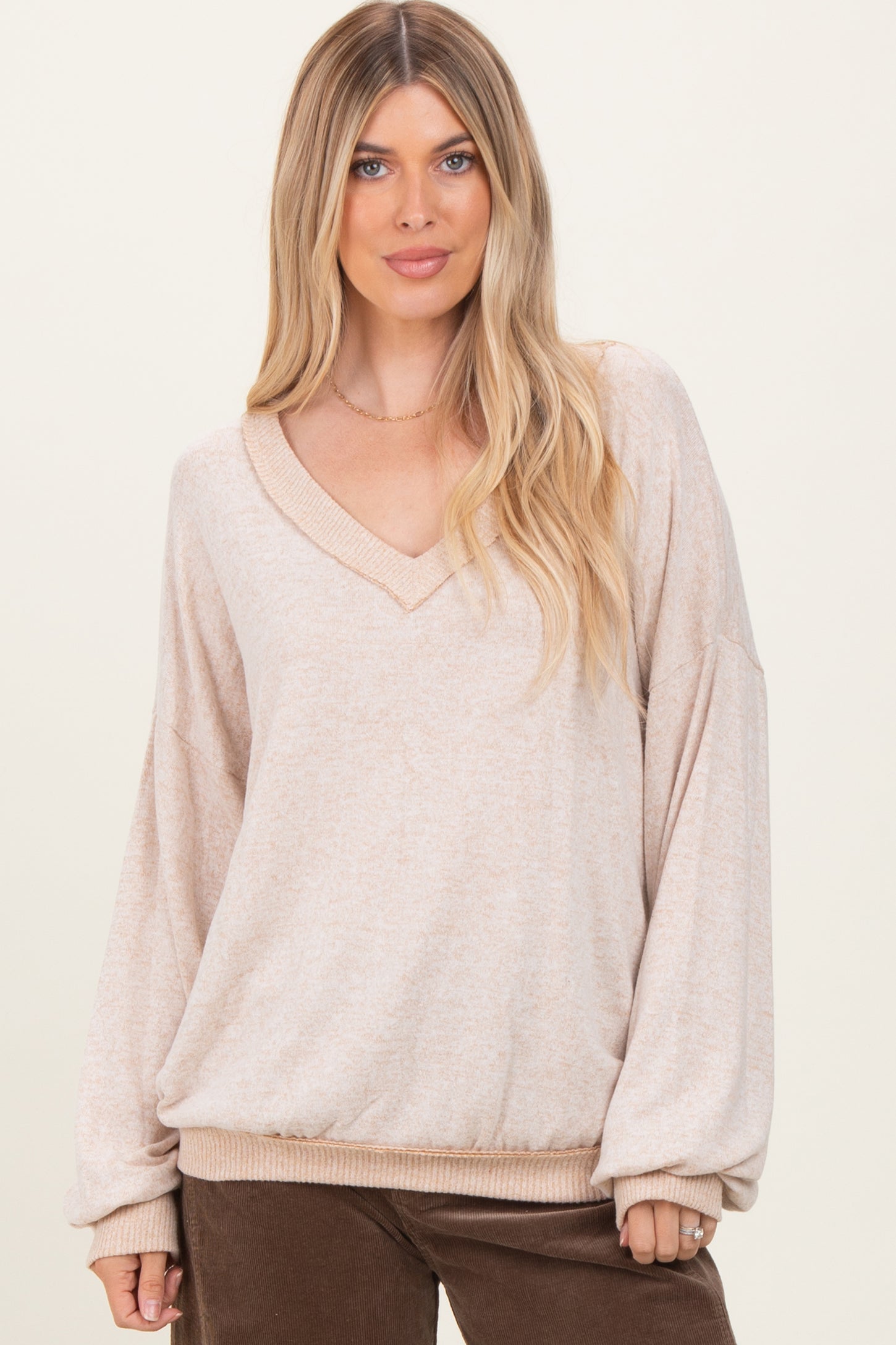 woman wearing a light beige oversized v-neck sweater with balloon sleeves and ribbed hem