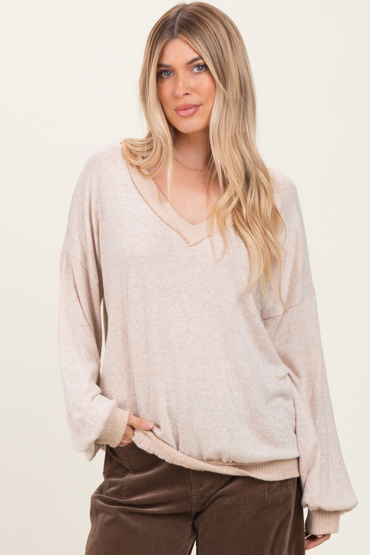 woman wearing a beige oversized v-neck long sleeve top with loose sleeves and side pockets