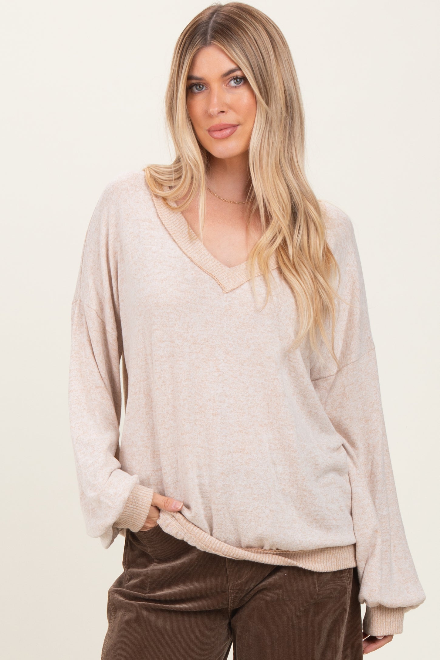 woman wearing a beige oversized v-neck long sleeve top with loose sleeves and side pockets