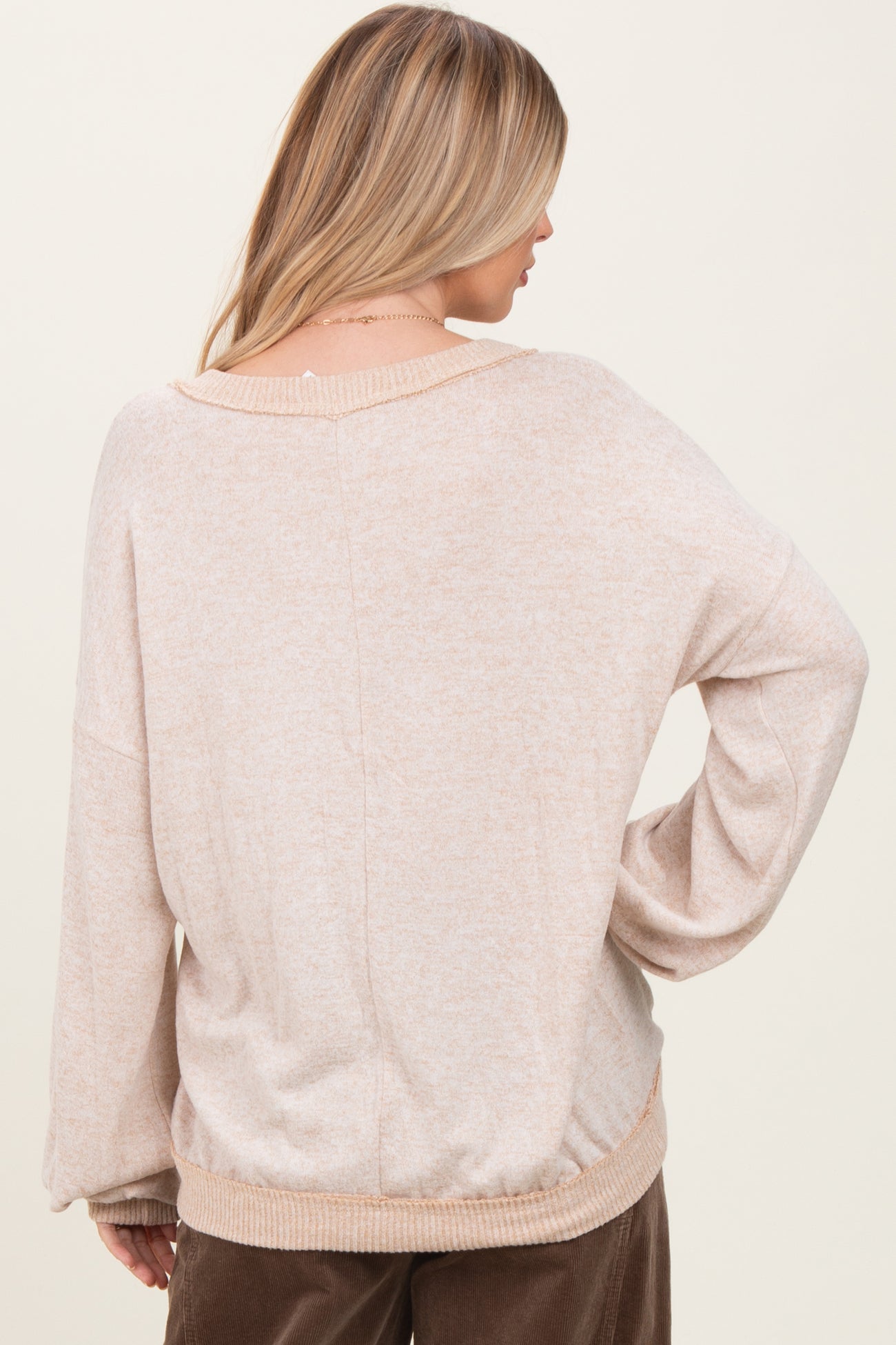 woman wearing a beige oversized sweater with a cinched hem and dropped shoulder seams