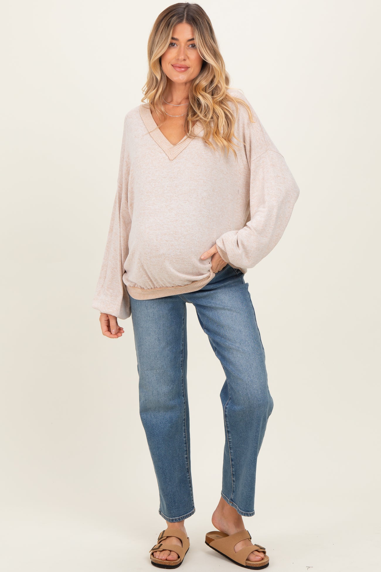 woman wearing a light pink oversized v-neck maternity sweater and jeans, showing her baby bump