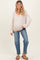 woman wearing a light pink oversized v-neck maternity sweater and jeans, showing her baby bump