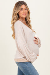 woman wearing a beige long sleeve maternity top and holding her baby bump