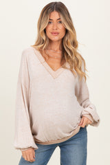 woman wearing a light beige maternity sweater with a v-neck and balloon sleeves, showing her baby bump