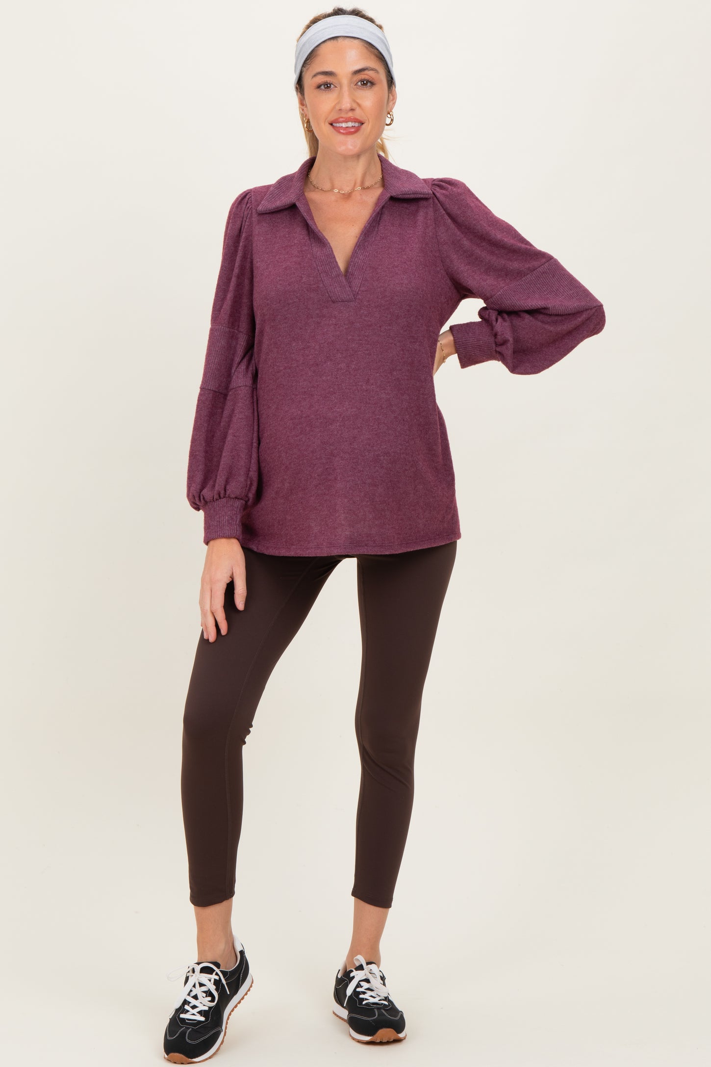woman wearing a maroon long sleeve maternity top with balloon sleeves and brown leggings, showing off her baby bump