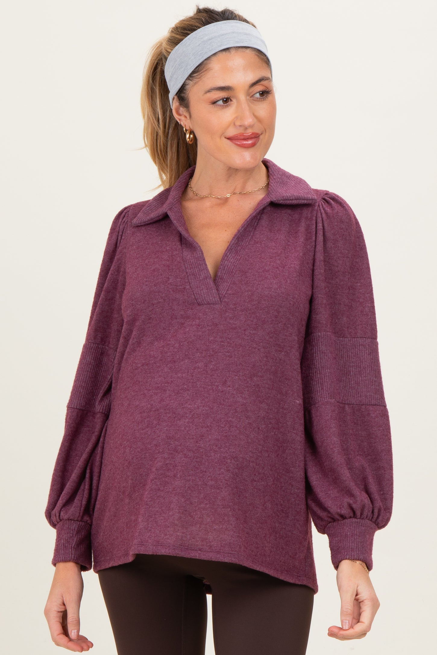 woman wearing a dark purple maternity pullover with balloon sleeves and a collared neckline, showing her baby bump
