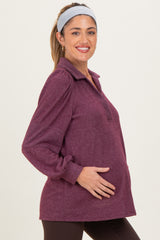 woman wearing a berry purple long sleeve maternity top with a collar and puff sleeves, holding her baby bump