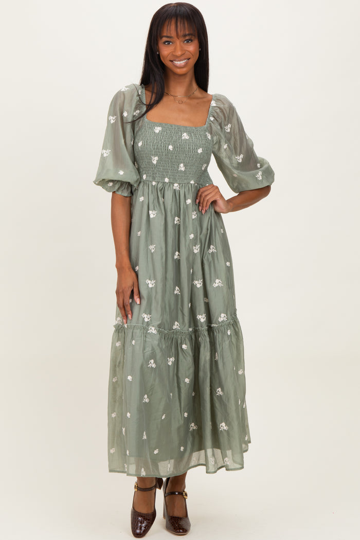 woman wearing a green floral embroidered maxi dress with puff sleeves and a fitted bodice