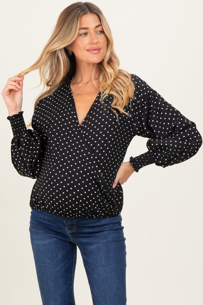 woman wearing a black maternity wrap blouse with white polka dots and puff sleeves, smiling and posing with one hand in her hair