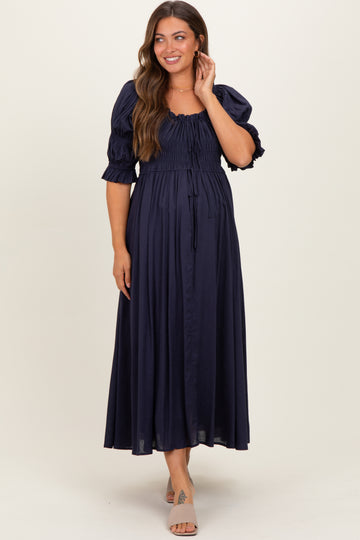 woman wearing a navy blue maternity maxi dress with puff sleeves and a smocked bodice, showing her baby bump