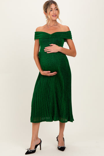 woman wearing a green off-the-shoulder maternity dress with a pleated skirt and holding her baby bump