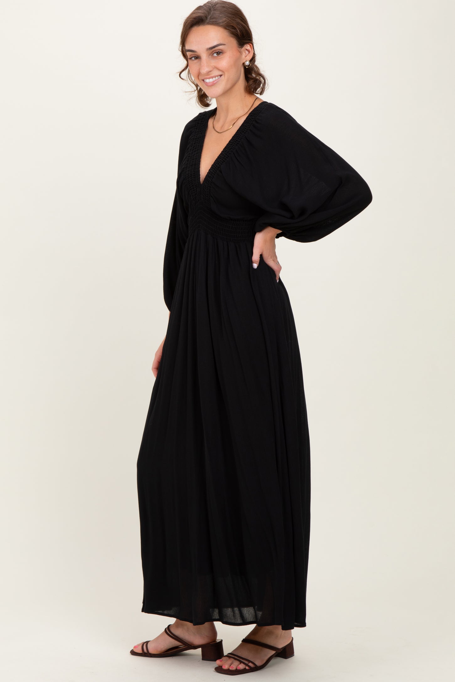 woman wearing a black maxi dress with a deep v-neck and puff sleeves, standing sideways with a flowing skirt