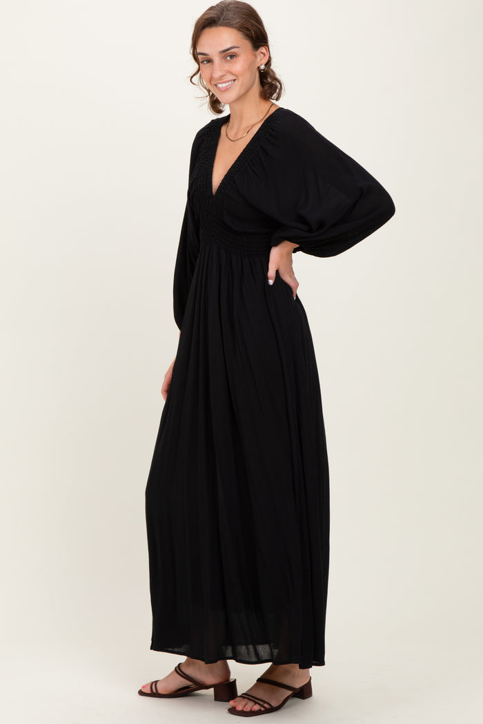 woman wearing a black maxi dress with a deep v-neck and puff sleeves, standing sideways with a flowing skirt