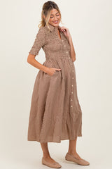 woman wearing a brown and white gingham maternity dress with short sleeves and pockets, highlighting her baby bump