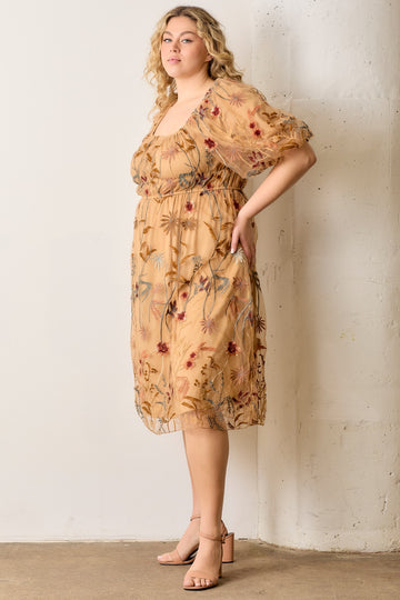 woman wearing a floral embroidered plus size dress with puff sleeves and a square neckline, standing against a wall