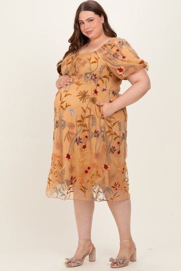 woman wearing a mustard yellow floral embroidered maternity dress with a cinched waist and puff sleeves, showing her baby bump