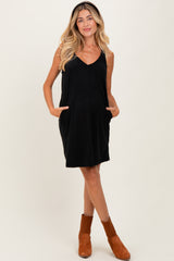 woman wearing a black sleeveless maternity dress with pockets and a v-neckline, showing her baby bump