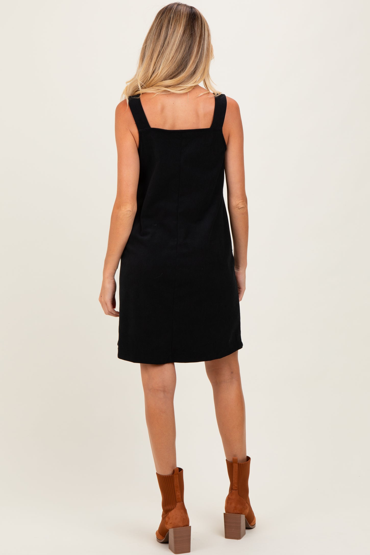 woman wearing a black maternity dress with thick straps and back detailing, styled with brown ankle boots