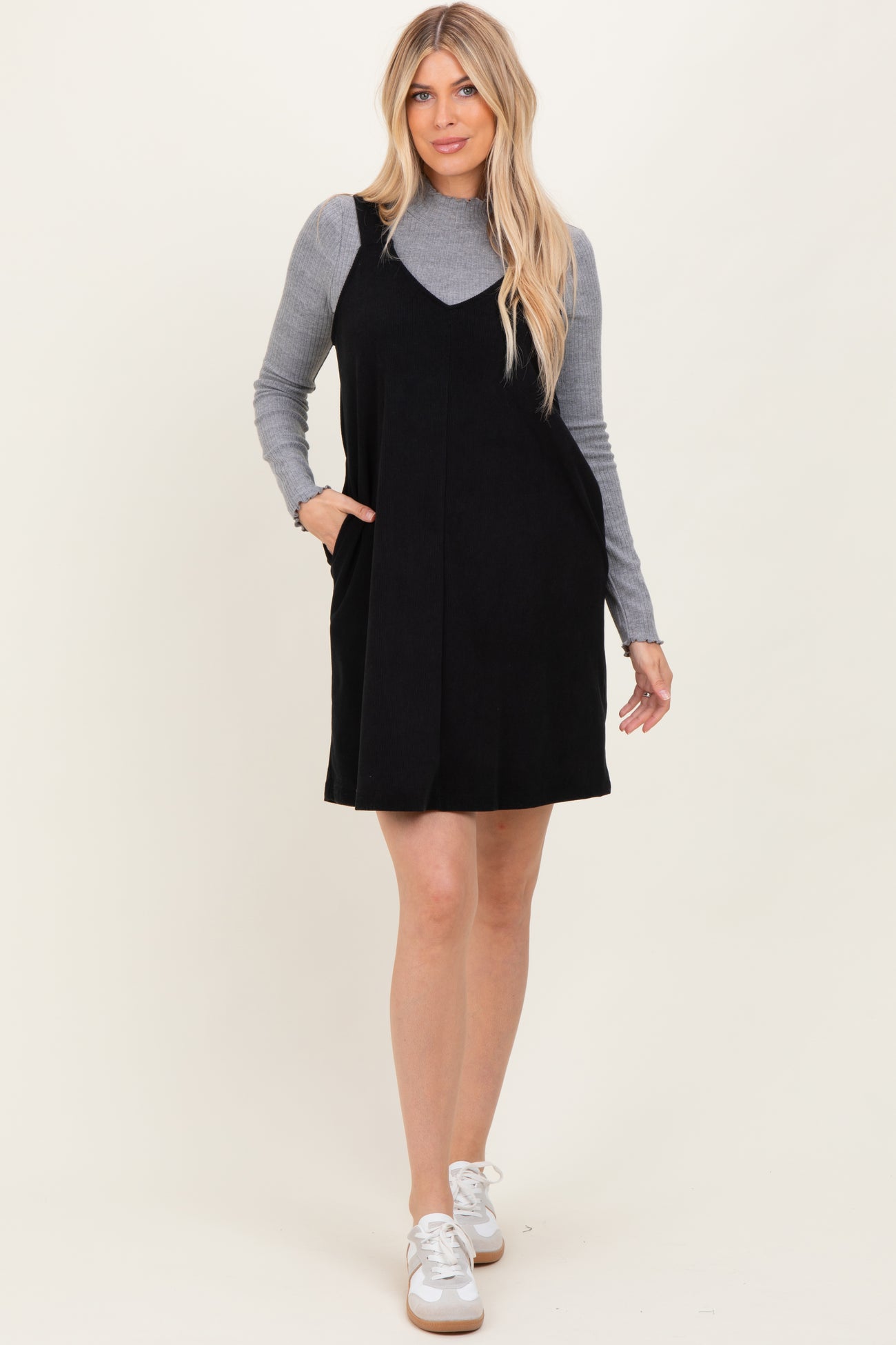 woman wearing a black suede slip dress over a gray long sleeve top with pockets and white sneakers
