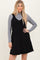 woman wearing a black corduroy overall dress over a gray long sleeve top
