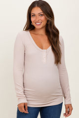 woman wearing a light beige long sleeve maternity top with a v-neck and button details, showing her baby bump