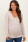 woman wearing a light beige long sleeve maternity top with a v-neck and button details, showing her baby bump