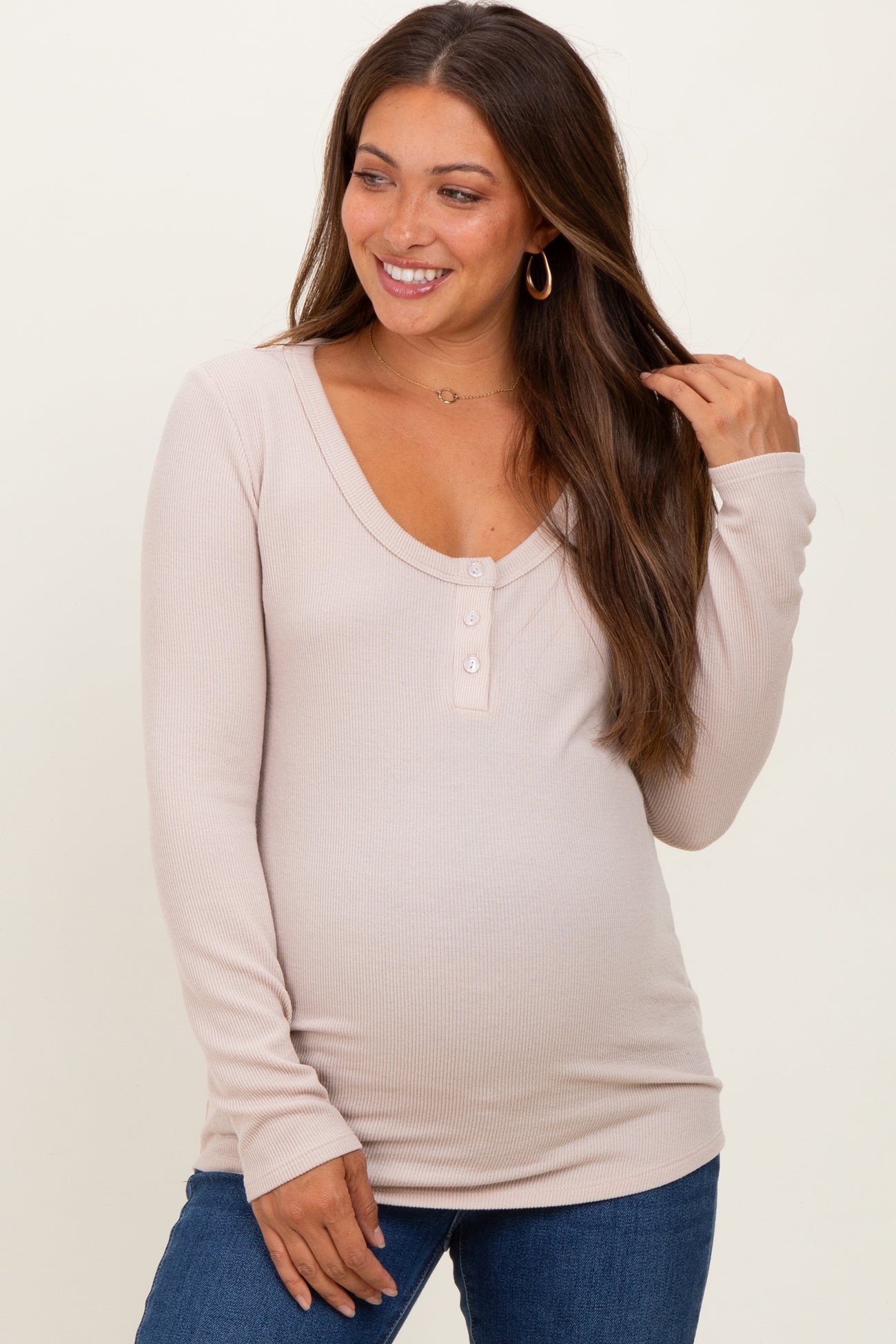 woman wearing a light beige long sleeve maternity top with button details and a visible baby bump