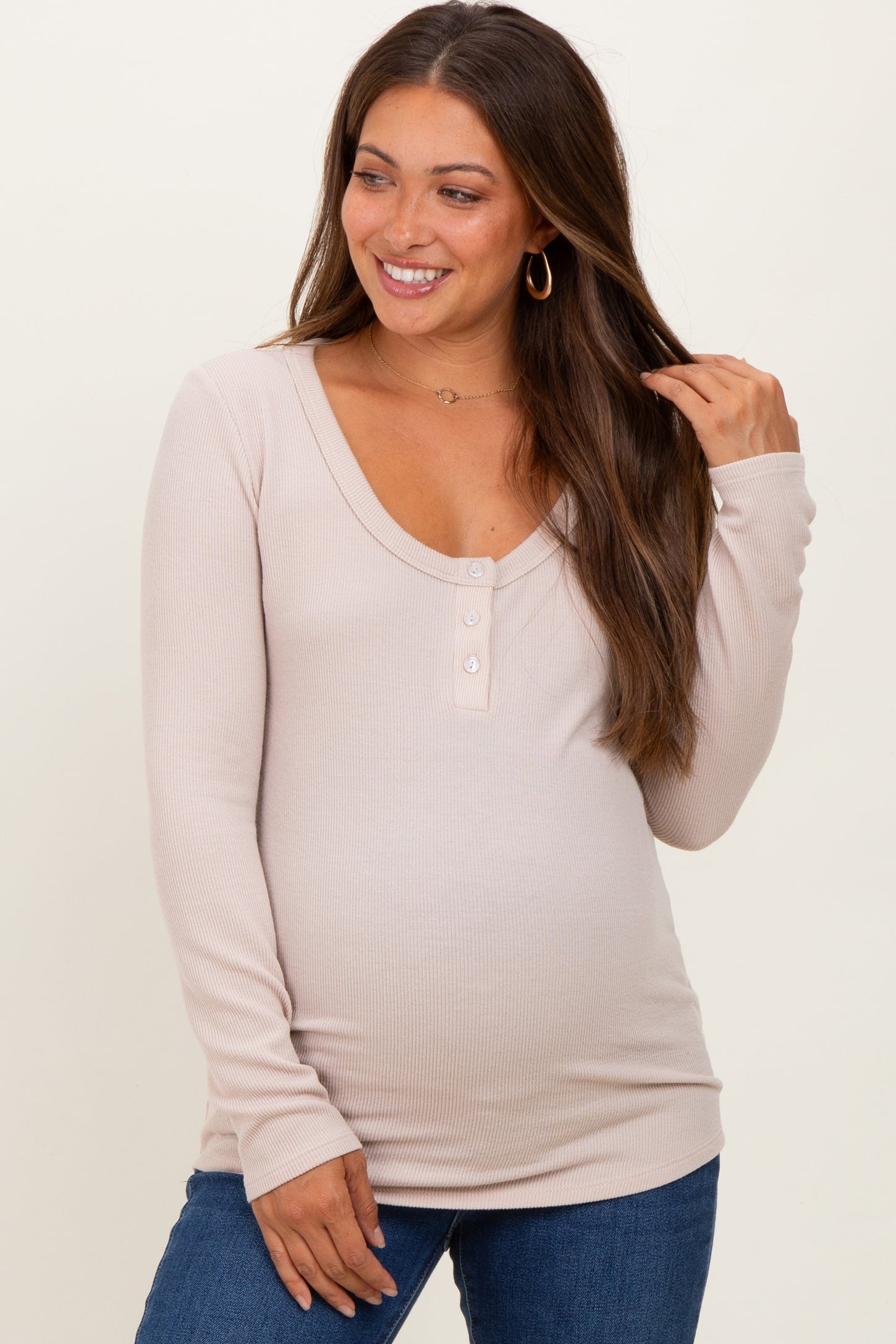 woman wearing a light beige long sleeve maternity top with button details and a visible baby bump