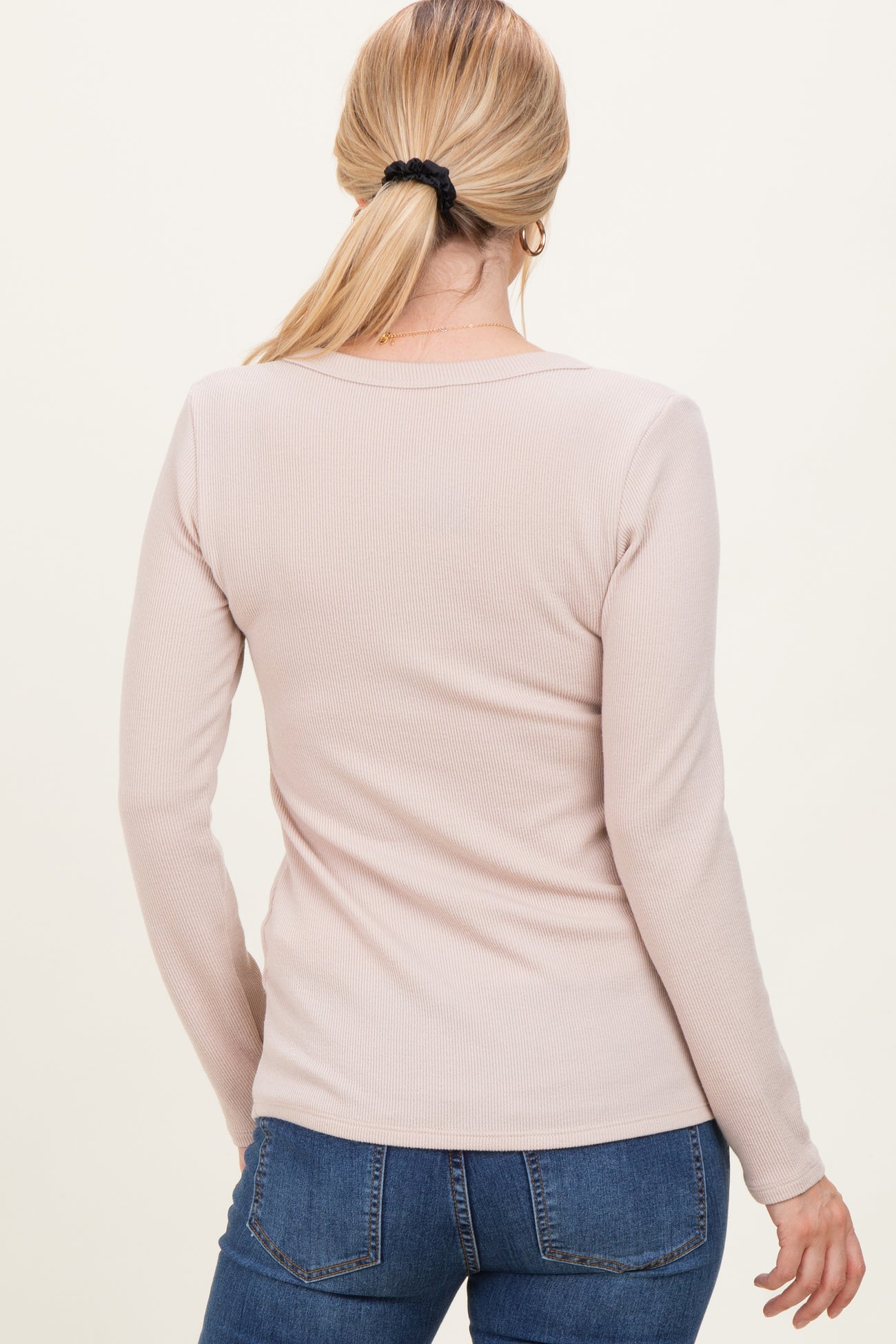 woman wearing a light pink long sleeve ribbed top, viewed from the back, paired with blue jeans