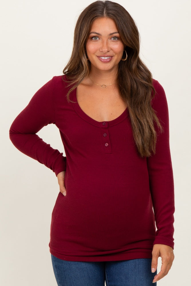 woman wearing a burgundy long sleeve maternity top with a scoop neckline and button details, showing her baby bump