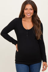woman wearing a black long sleeve maternity top with a scoop neck and button details, showing her baby bump