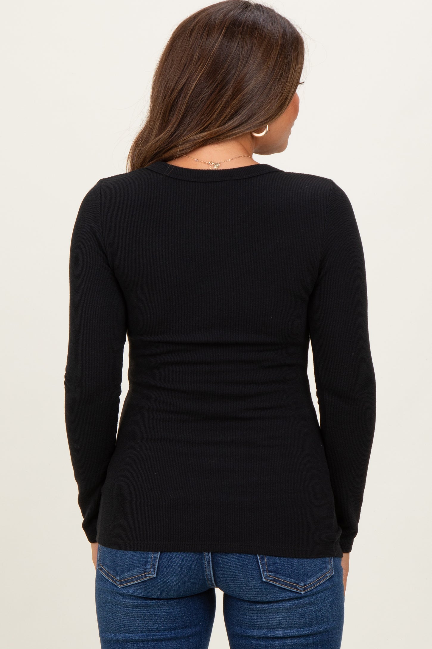 woman wearing a black long sleeve maternity top, seen from the back, paired with blue jeans