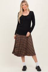 woman wearing a black long sleeve henley top with a brown pleated checked midi skirt and black chunky loafers