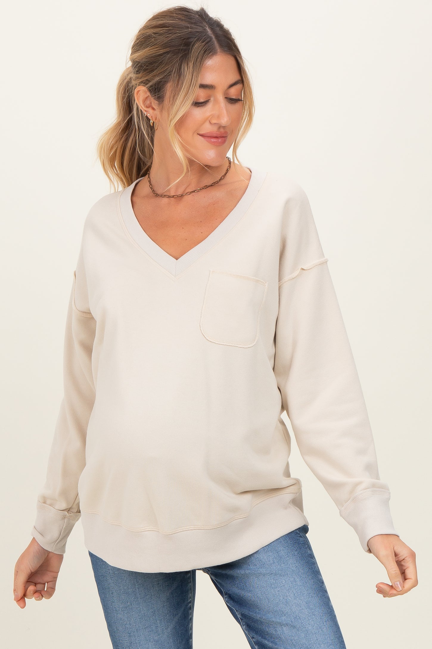 woman wearing a beige v-neck maternity sweatshirt with a pocket and a visible baby bump