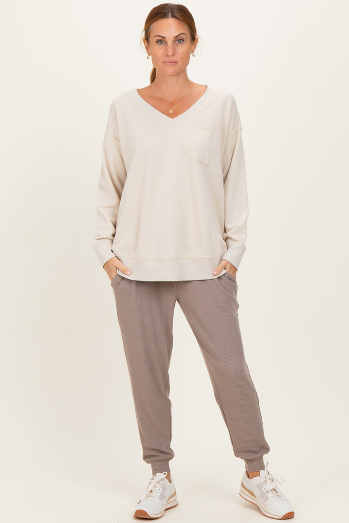 woman wearing a light beige long sleeve v-neck sweatshirt with a pocket and gray ribbed jogger pants