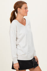 woman wearing a light gray v-neck sweatshirt with a pocket and black denim skirt
