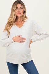 woman wearing a beige maternity sweatshirt with a v-neck and pocket, holding her baby bump