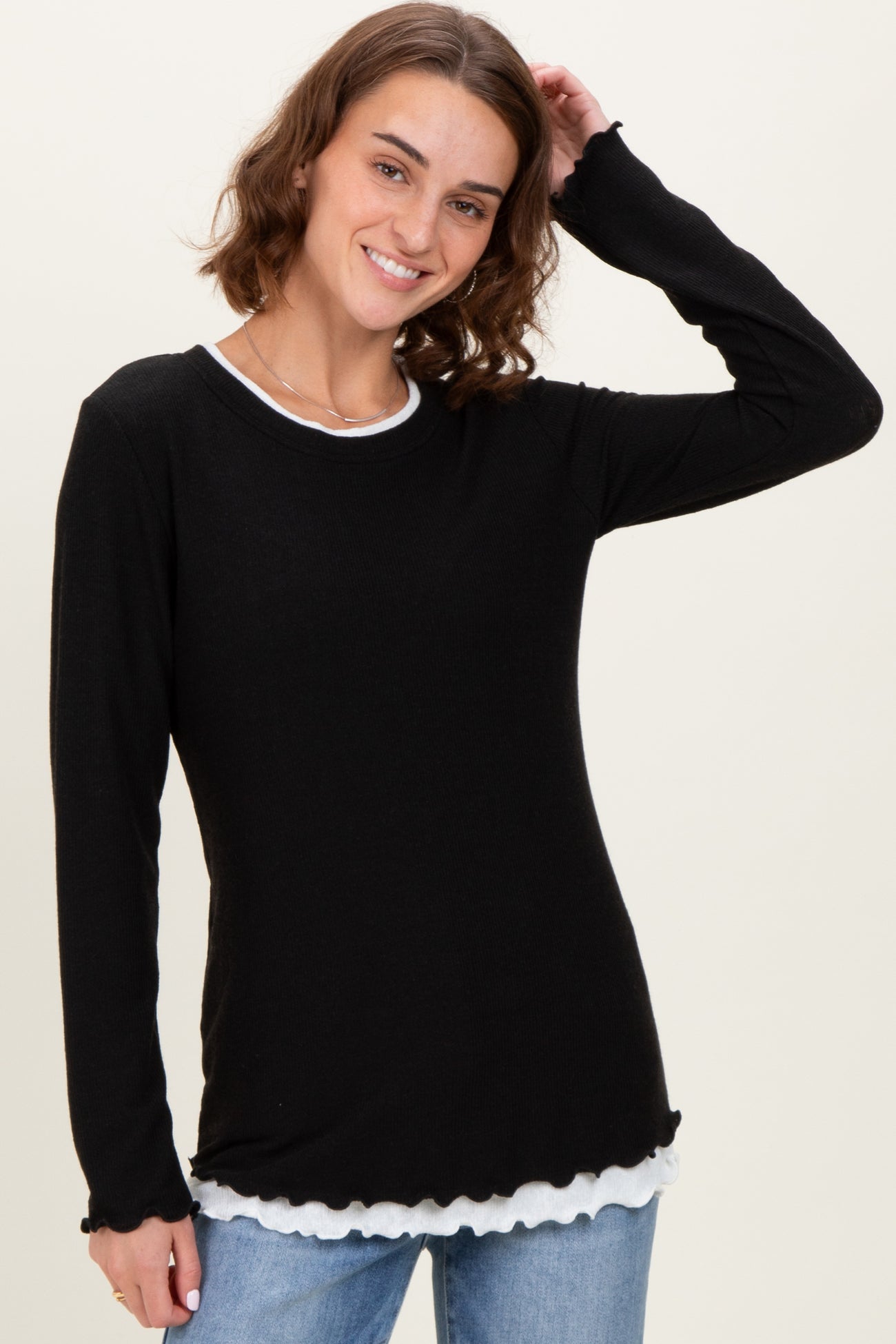 woman wearing a black long sleeve top with scalloped hem and a white inner layer showing at the neckline and bottom