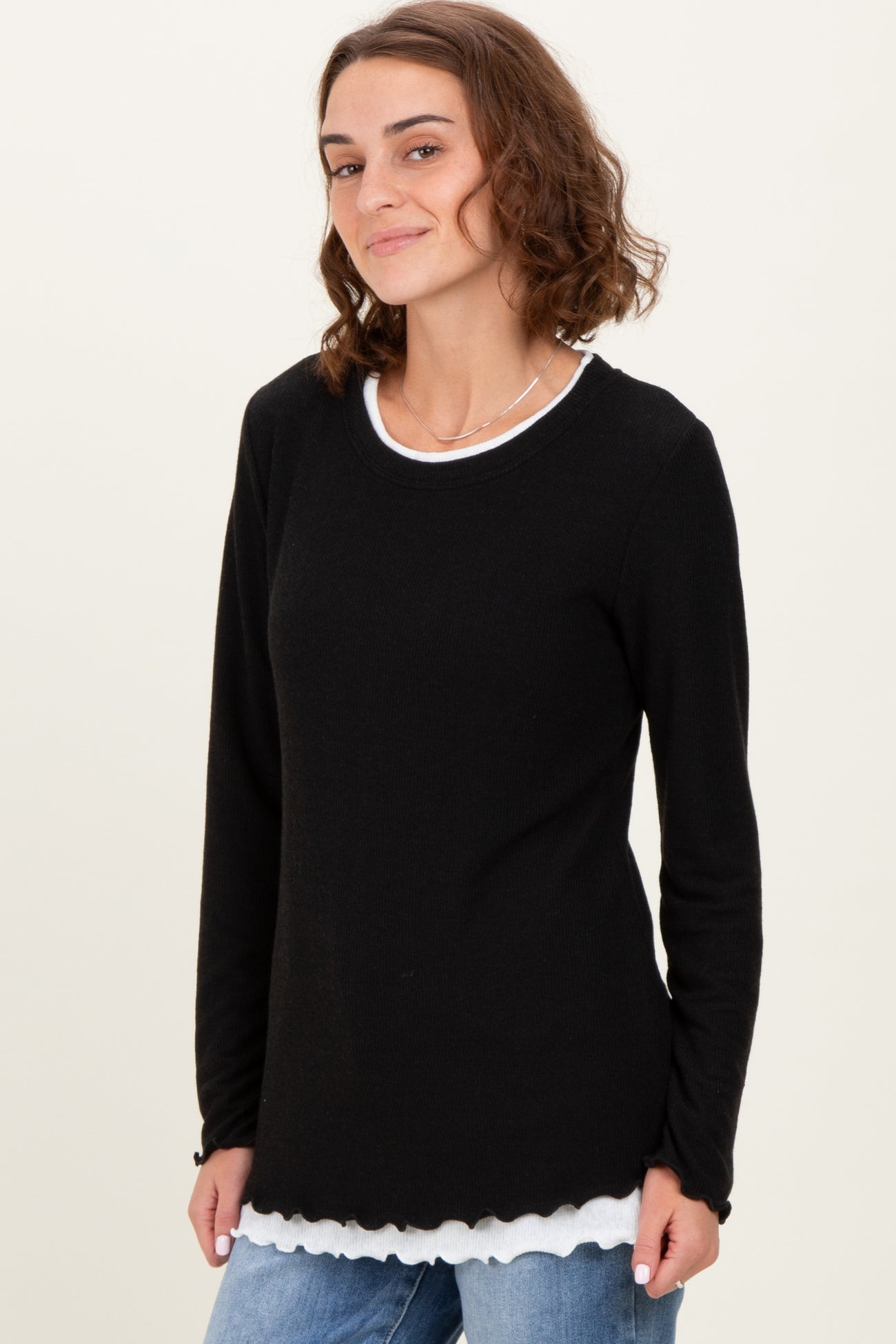 woman wearing a black long sleeve top with a scalloped hem over a white shirt, smiling at the camera
