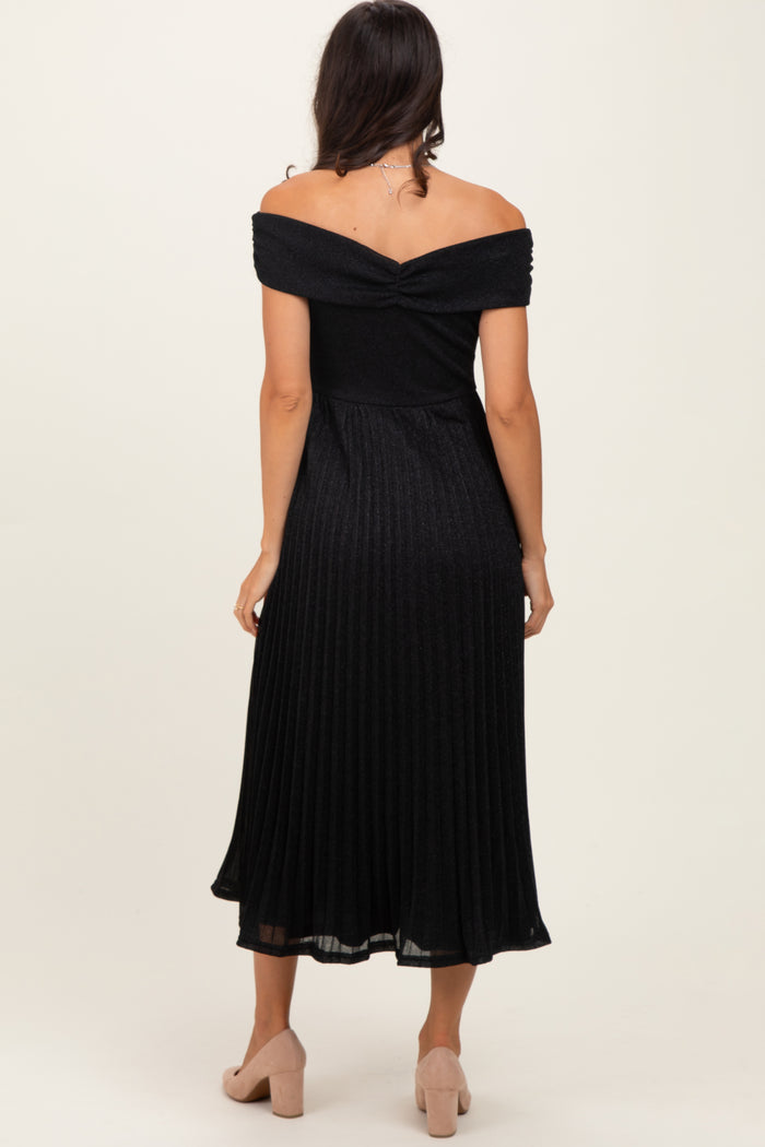 woman wearing a black off-the-shoulder pleated midi dress, showing the back view and styled with light-colored heels