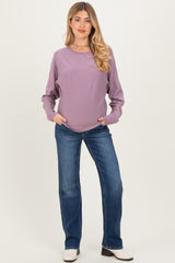 woman wearing a mauve long sleeve maternity top and blue straight leg jeans with hands in pockets and visible baby bump