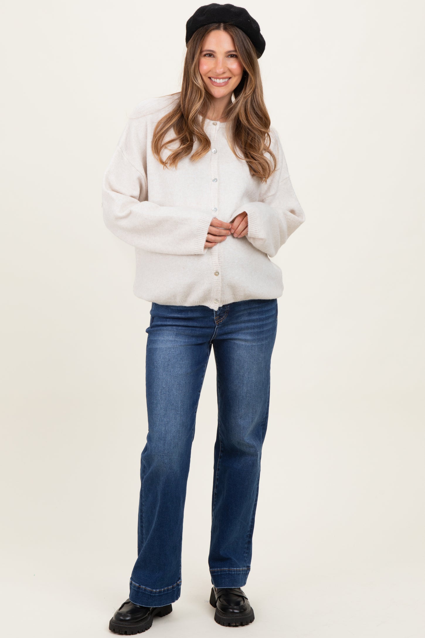 woman wearing a cream oversized button-up maternity jacket with wide sleeves and blue flared jeans