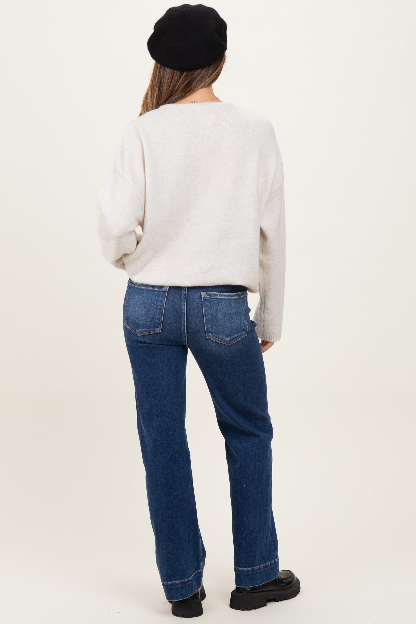 woman wearing a light gray maternity sweater and blue jeans, showing her back with loose fit and straight legs
