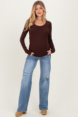woman wearing a burgundy long sleeve maternity top with side pockets and distressed blue jeans, showing her baby bump