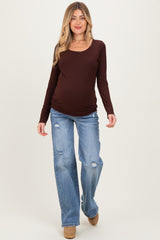 woman wearing a brown long sleeve maternity top and distressed light blue jeans, showcasing her baby bump